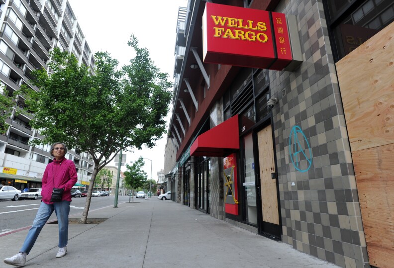 A woman walks by a damaged Wells Fargo branch in downtown Oakland, California on May 02, 2015. Hundreds marched throughout the city on May 1 to mark International Workers' Day vandalizing store fronts, smashing windows and lighting a car on fire before eventually dispersing.    AFP PHOTO/JOSH EDELSON        (Photo credit should read Josh Edelson/AFP/Getty Images)