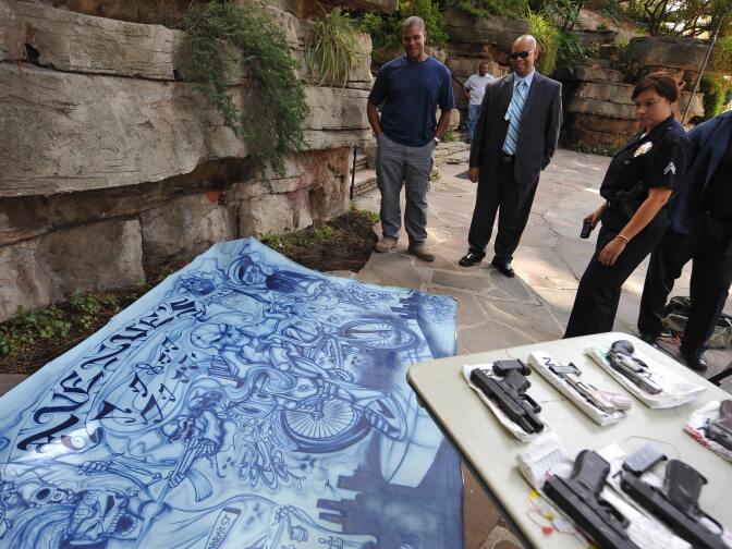 Police officers look at a large painting confiscated from a raided home of alleged Avenues gang member is on display at a press conference to announce the massive early-morning raid by hundreds of police officers and federal law enforcement agents against the notorious gang, in Los Angeles, CA on September 22, 2009.  