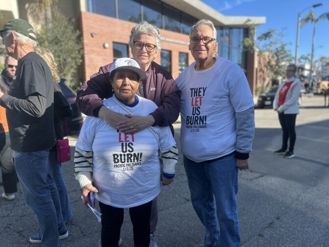 Three people stand together. Two wear T-shirts that read "They let us burn."