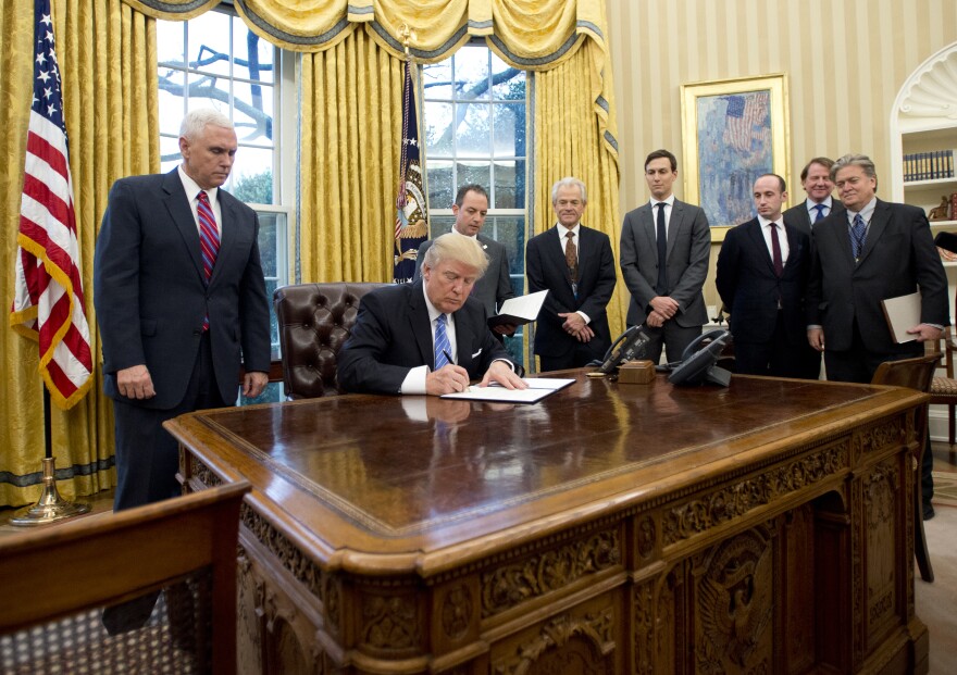 WASHINGTON, DC - JANUARY 23:  (AFP OUT) U.S. President Donald Trump signs the first of three Executive Orders in the Oval Office of the White House in Washington, DC on Monday, January 23, 2017.  They concerned the withdrawal of the United States from the Trans-Pacific Partnership (TPP), a US Government hiring freeze for all departments but the military, and "Mexico City" which bans federal funding of abortions overseas.  Standing behind the President, from left to right: US Vice President Mike Pence; White House Chief of Staff Reince Preibus; Peter Navarro, Director of the National Trade Council; Jared Kushner, Senior Advisor to the President; Steven Miller, Senior Advisor to the President; unknown; and Steve Bannon, White House Chief Strategist. (Photo by Ron Sachs - Pool/Getty Images)
