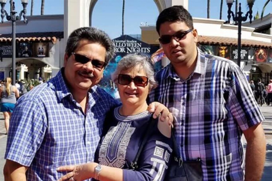 A father mother and grown son, all dressed in patterned blue shirts, stand inside Universal Studios theme park. Banners behind them tout Halloween Horror Nights.