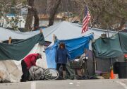 Two people standing in front of tents and homeless encampments.