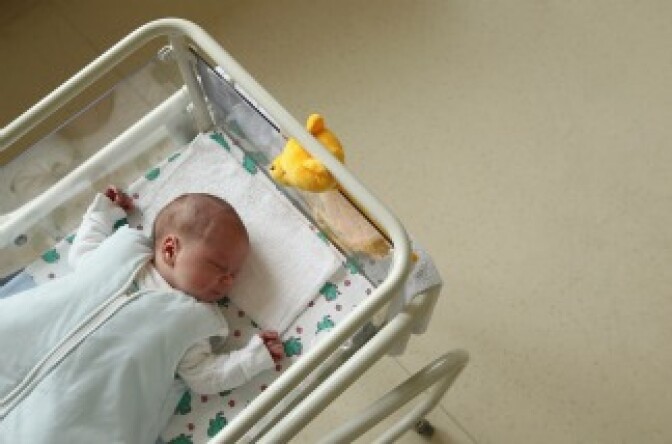A newborn baby lies in bed in a hospital maternity ward.