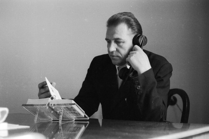 A man flips through his desk diary while talking on the telephone on May 18, 1961.