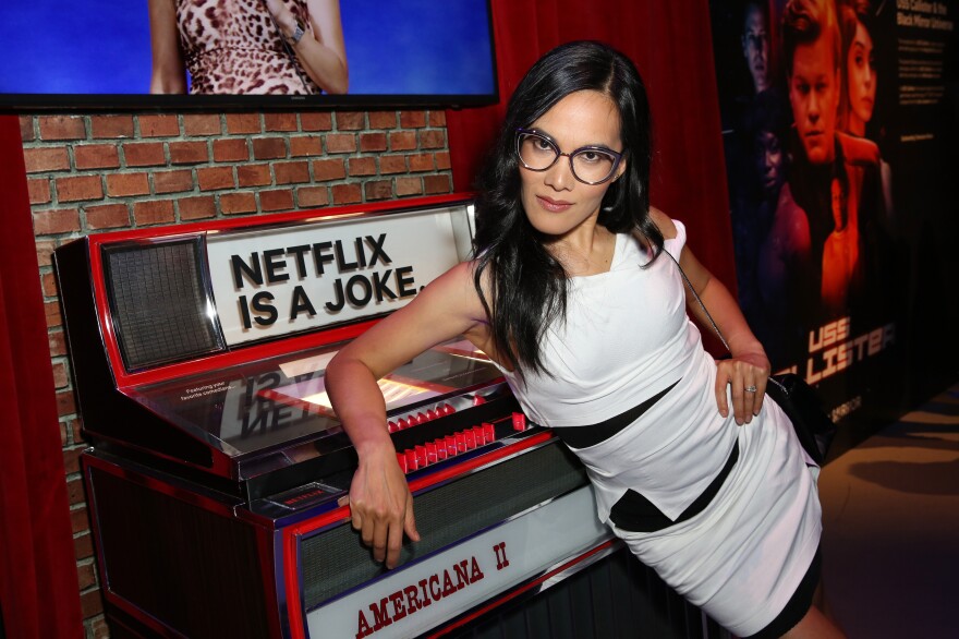 Ali Wong leans against a jukebox with Netflix Is a Joke branded on the top. She's wearing a white and black dress.