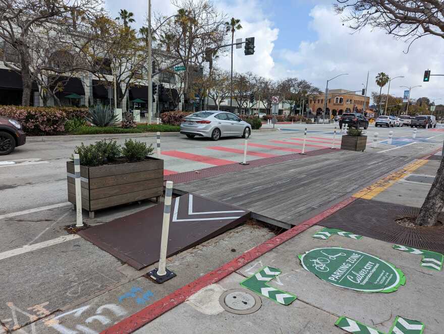 A car in one lane on the street. Another lane is marked in red stripes. And a wooden platform is next to the curb. A green circle on the floor reads "Parking Zone" for bicyclists.