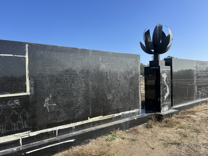 A diagonal view of a black granite wall with the outline of names vaguely visible on the surface and an internal flame in the center with a map of Vietnam engraved on it. 