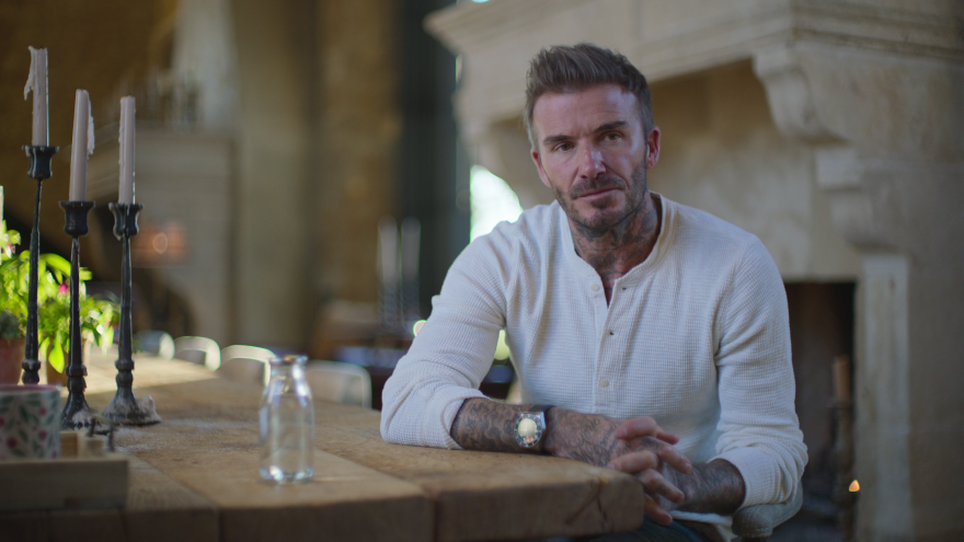 Man, sitting down and arm rested on a table, looks off to the distance.