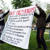 Several young people hold up a large white sign that reads "OUR DEMANDS".