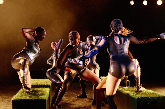 A group of Black dancers wearing black outfits perform on stage. 