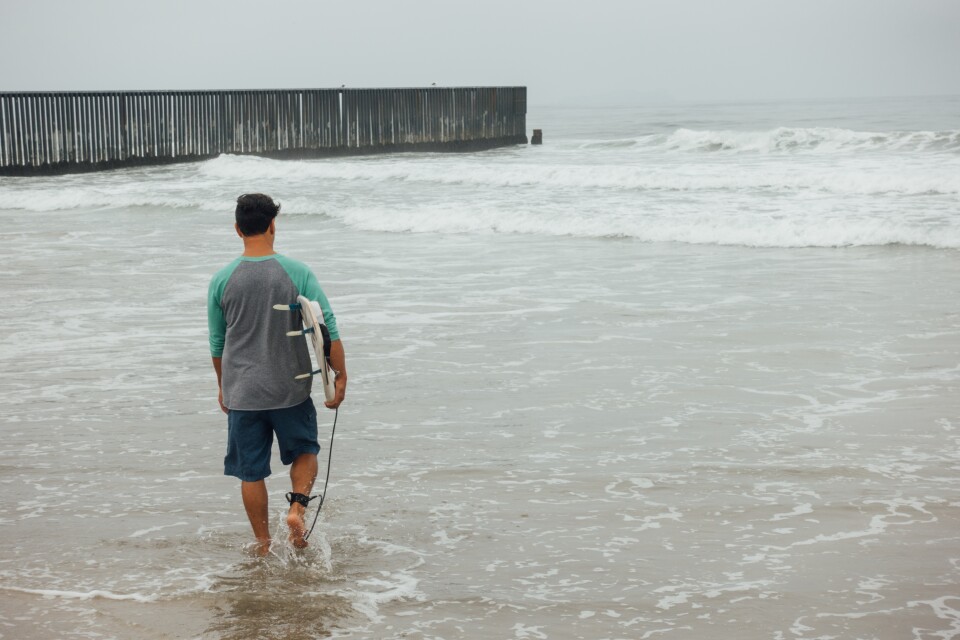 L.A. artist Diego Palacios heads out to surf at the border between the U.S. and Mexico on August 12th, 2017. The Beach at Border Field State Park in San Diego, CA is located in the farthest Southwest corner of the United States, separated from Playas de Tijuana by an 18-foot high fence.