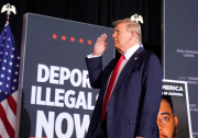 Man in a navy suit and red tie salutes. There is an American flag and sign that reads in bold "Deport illegals now"