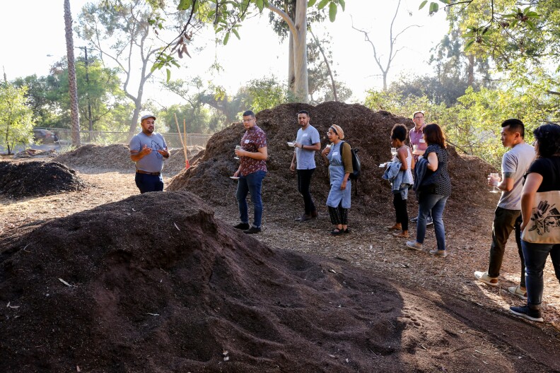 A group of people walk among large piles of dirt on a sunny day.