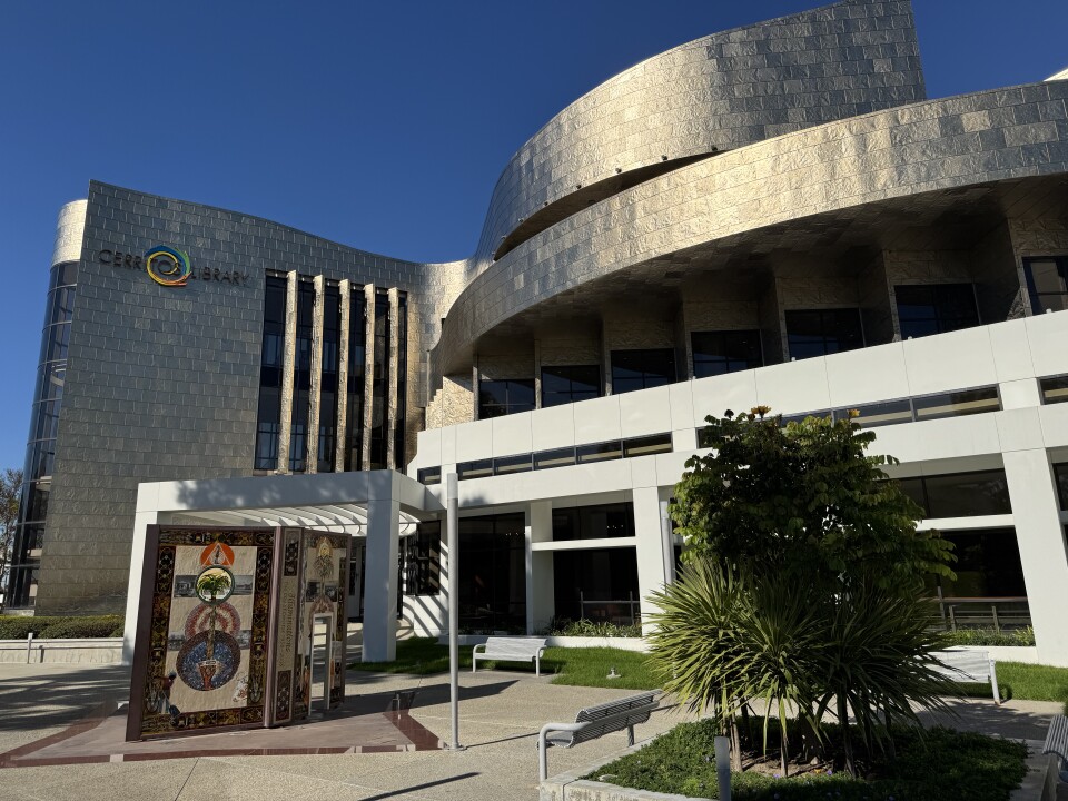 The exterior of a modern institutional building with distinctive architectural features and an outdoor art element.
The building has a contemporary design with a curved facade clad in light-colored stone or textured panels.
