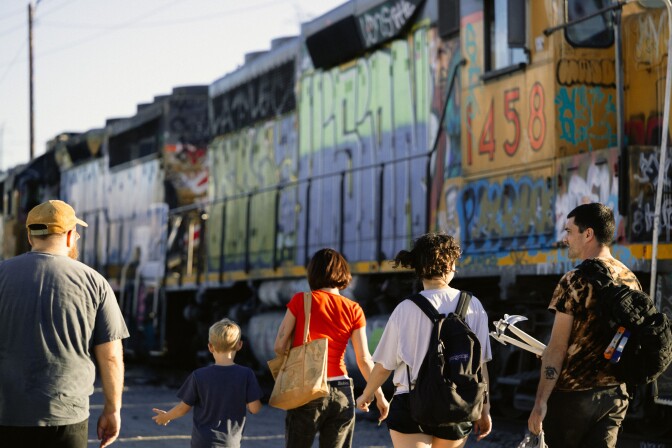 A small group of people, including a child, walk by a train with graffiti spray on it.