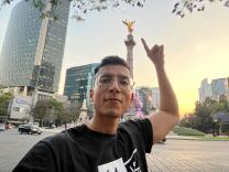 A young Latino man with glasses in Mexico City in front of the Angel de Independencia