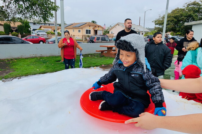 small boy on a disc-style sled sliding on snow as an adult's arms guide him.