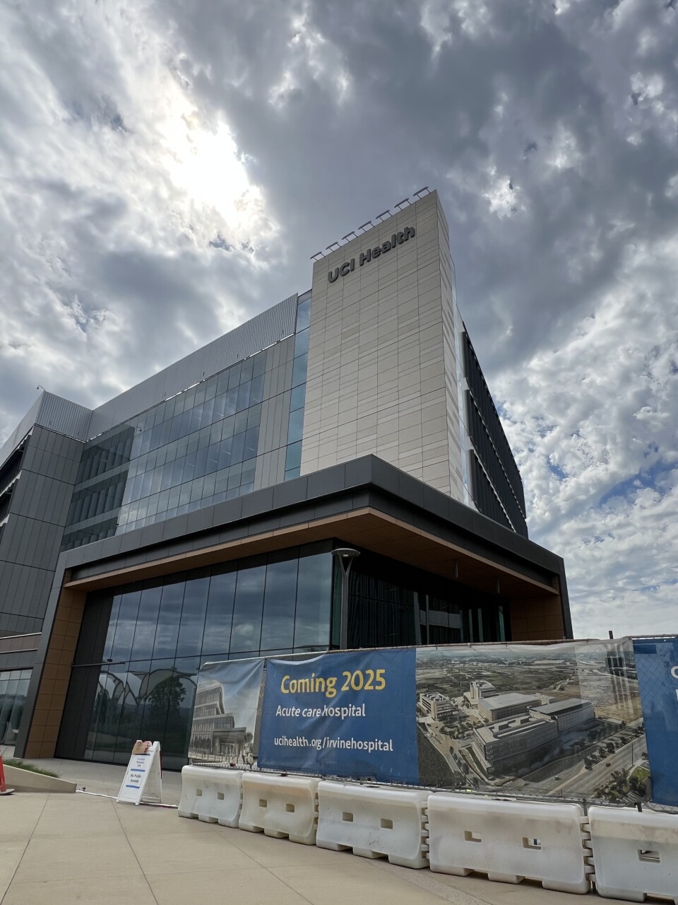 A grey, brown and beige building with the words UCI Health Coming 2025 on a cloudy day. 
