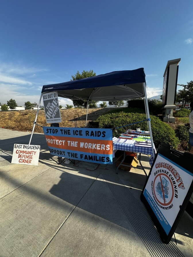 A table with signs and informational material is set up on a sidewalk.