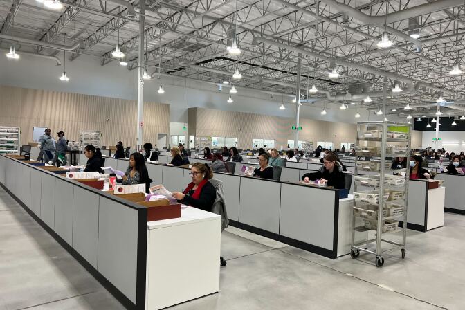 People process votes at long white desks in a warehouse room