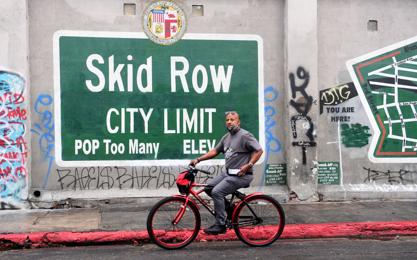 A map on a red bicycle rides past the sign that reads: Skid Row City Limit. POP Too Many.