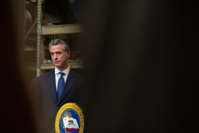 A man in a suit wearing a blue tie stands in front of a podium that says state of california