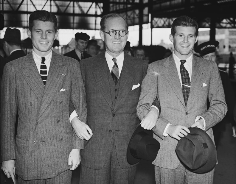 three men stand there, wearing suits, linking arms