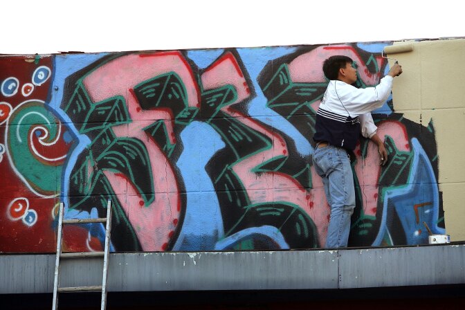 A man paints over graffiti on top of a business on November 1, 2006 in the Koreatown section of Los Angeles, California.