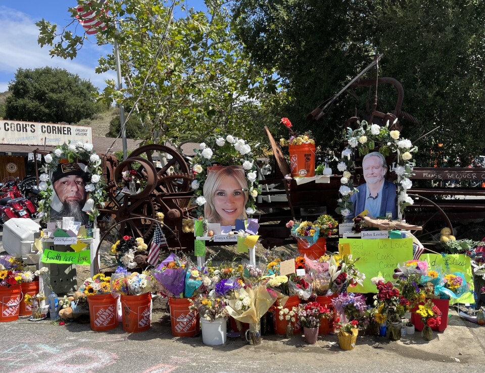 A close-up look at the makeshift memorial outside Cook's Corner, site of a mass shooting that killed three: Home Depot buckets are overflowing with bouquets of flowers. There are flags, signs, notes and three large photos of the victims who died. 
