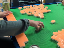 A hand reaching for a Chinese mahjong game tile on top of a table.