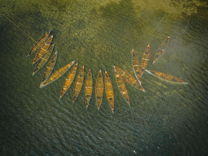An aerial shot of a cluster of canoes in a lake.