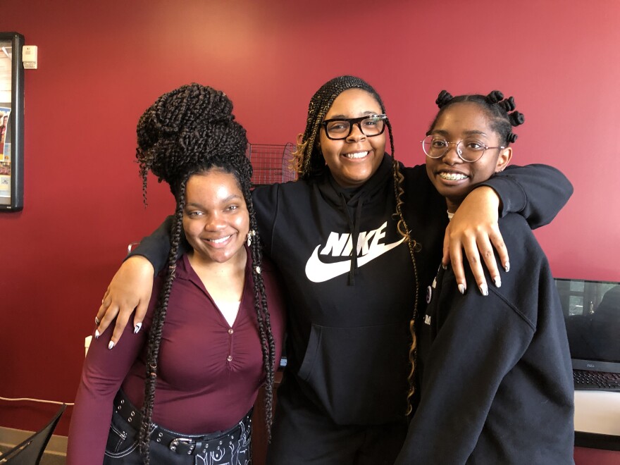 Three Black college women embrace and smile at the camera.