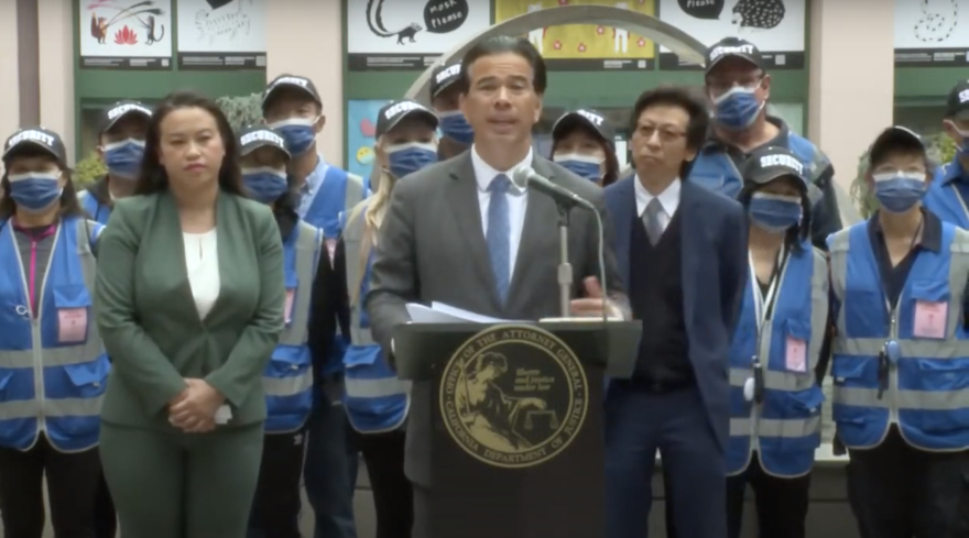 California Attorney General Rob Bonta stands in front of a group of people wearing blue vests and masks in Oakland's Chinatown for his press conference on hate crimes.