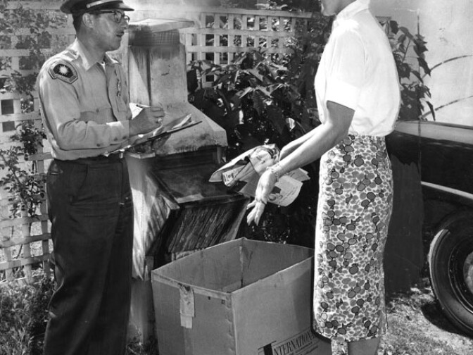 "Patrolman Terzo explains to a new resident that incinerator burning has been been banned within the Los Angeles basin since Sept. 30, 1957, and that the fire should be extinguished immediately. Photo dated: June 25, 1960." 