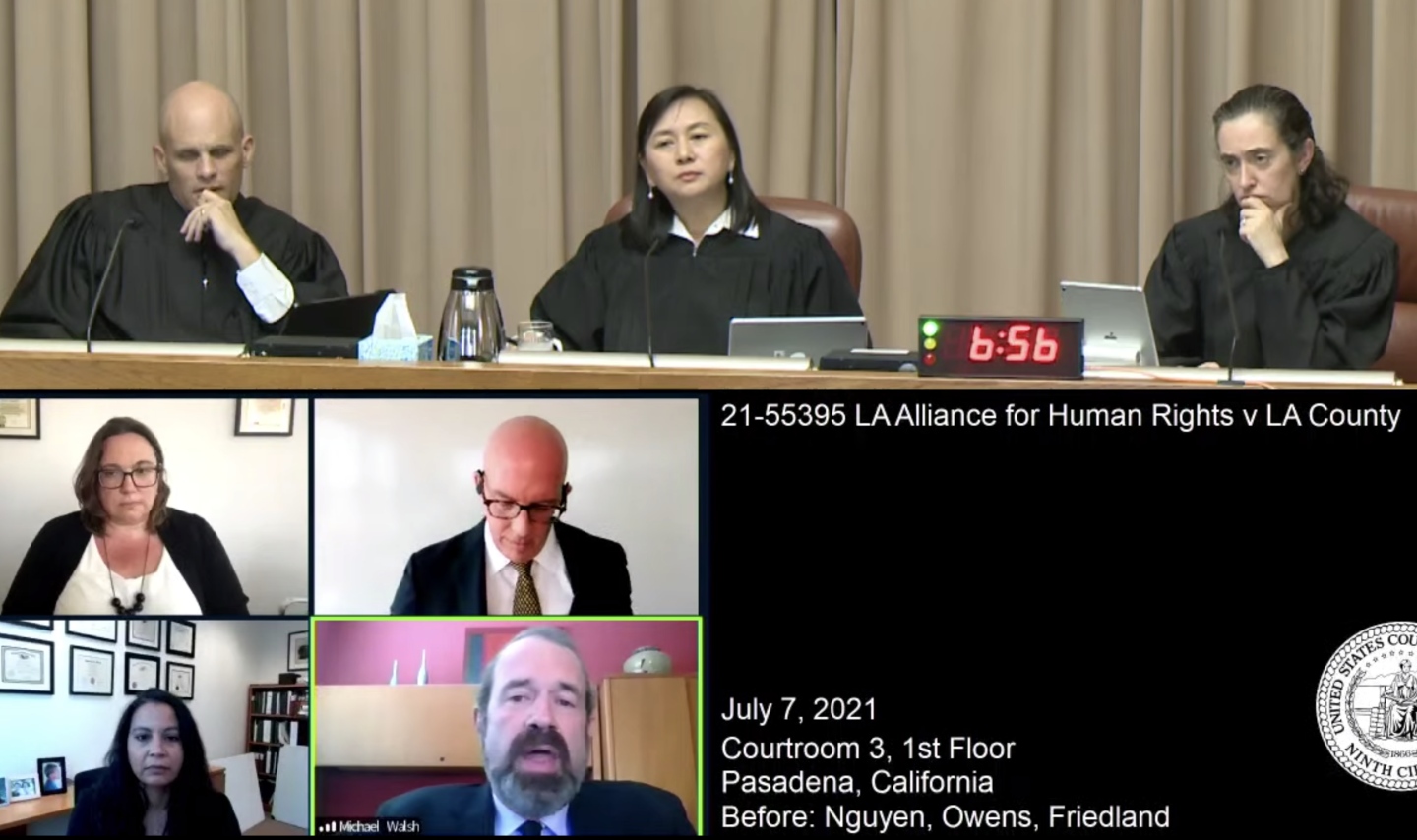 A video still frame of the Ninth Circuit Court's hearing; at the top, three judges wear black robes and sit behind a long desk. Beneath them, four attorneys appear via video conference from their respective offices.