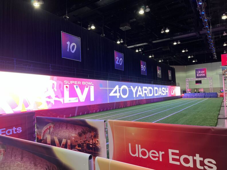 A skill activity set has running lanes marked off a green artificial turf surface by a large banner that says Super Bowl LVI and 40 Yard Dash on the left side and an Uber Eats advertisement banner in the foreground at the NFL Super Bowl Experience.