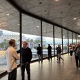 Museum attendees mill around the cement and glass interior of the David Geffen Galleries. In the background, illuminated street lights from the Urban Light public art installation are visible, along with palm trees and other museum buildings.