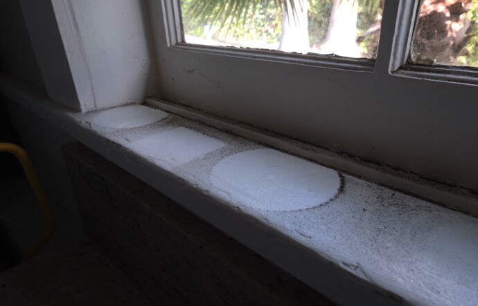 The outlines of plant pots are seen on a white window sill darkened by soot from the Eaton Fire. 
