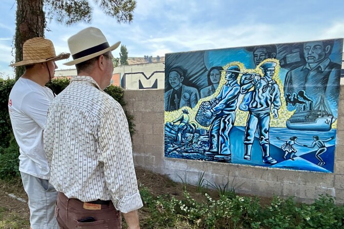 Two people wearing hats stand in front of a mural painted in blue.