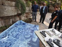 Police officers look at a large painting confiscated from a raided home of alleged Avenues gang member is on display at a press conference to announce the massive early-morning raid by hundreds of police officers and federal law enforcement agents against the notorious gang, in Los Angeles on Sept. 22, 2009.