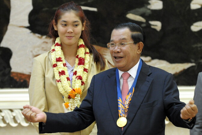File: Cambodian Prime Minister Hun Sen gestures as Sorn Seavmey (behind), Gold medal winner in the woman's 73kg Taekwondo at the 17th Asian Games in Incheon, South Korea, looks on during a victory ceremony at the Peace Palace in Phnom Penh, on Oct. 5, 2014.