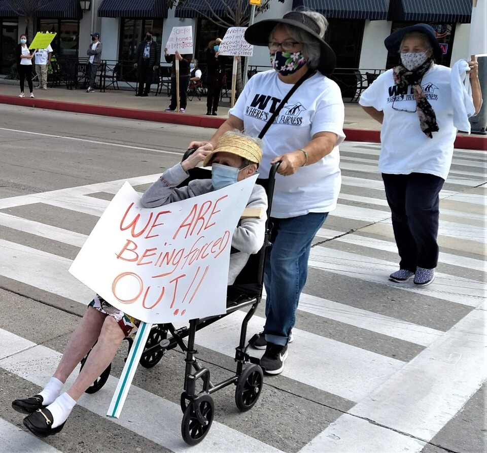 Person in a wheelchair holds a protest sign saying "we are being forced out".