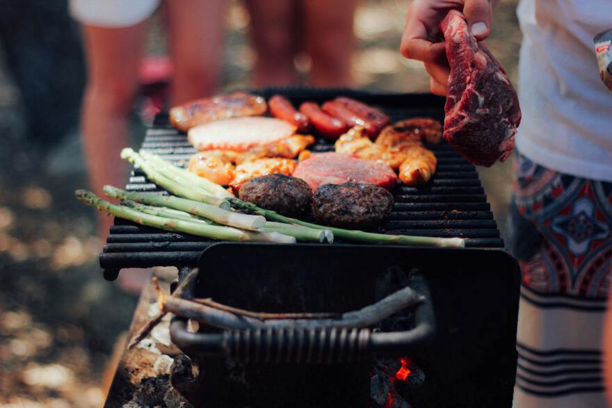 An assortment of hot dogs, steak, burgers, asparagus, and more on a grill.