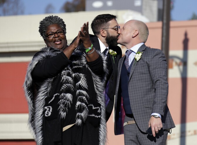 Aubrey Loots, right, and Danny Leclair, the first gay couple to be married aboard a float in the Tournament of Roses, kiss after being wed by the Rev. Alfreda Lanoix of the Unity Fellowship Church of Christ, left, aboard the AIDS Healthcare Foundation float in the 125th Rose Parade in Pasadena, Calif., Wednesday, Jan. 1, 2014. (AP Photo/Reed Saxon)
