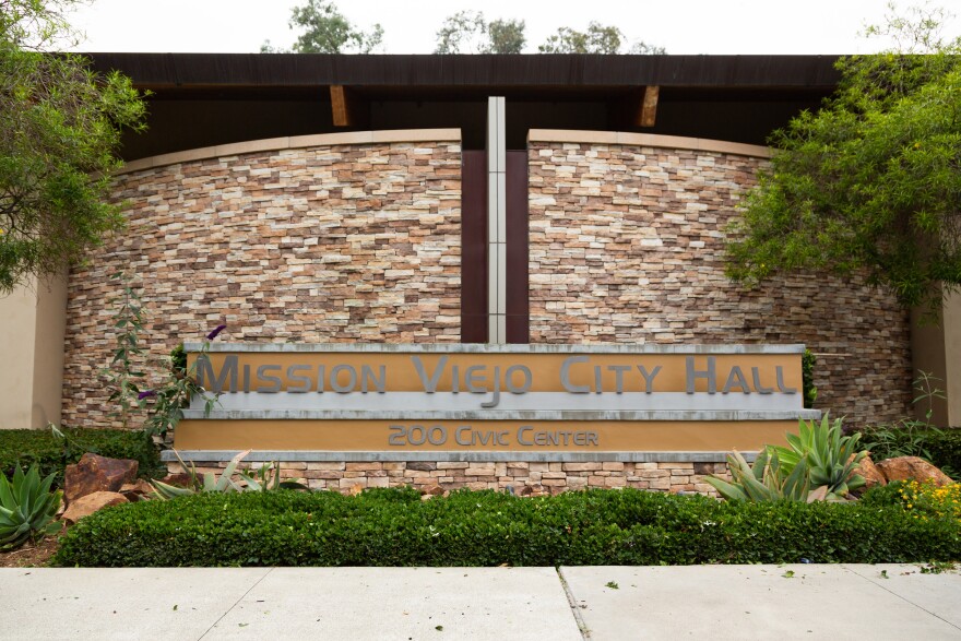 A curving, multi-colored brick wall with a concrete plaque across the front that reads "Mission Viejo City Hall."