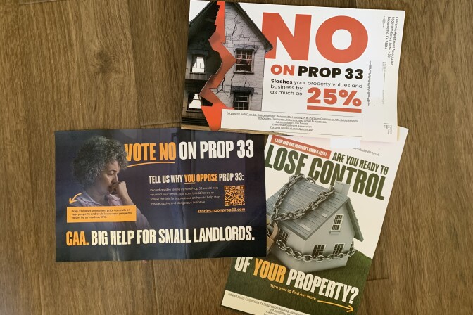 Three colorful mailers on a hardwood floor. One has a large picture of a house wrapped in chains with the words, "Are you ready to lose control of your property?" Another shows a somber woman with the word "Vote no on Prop 33." Another has the cracked facade of a building with the words "No on Prop 33." 