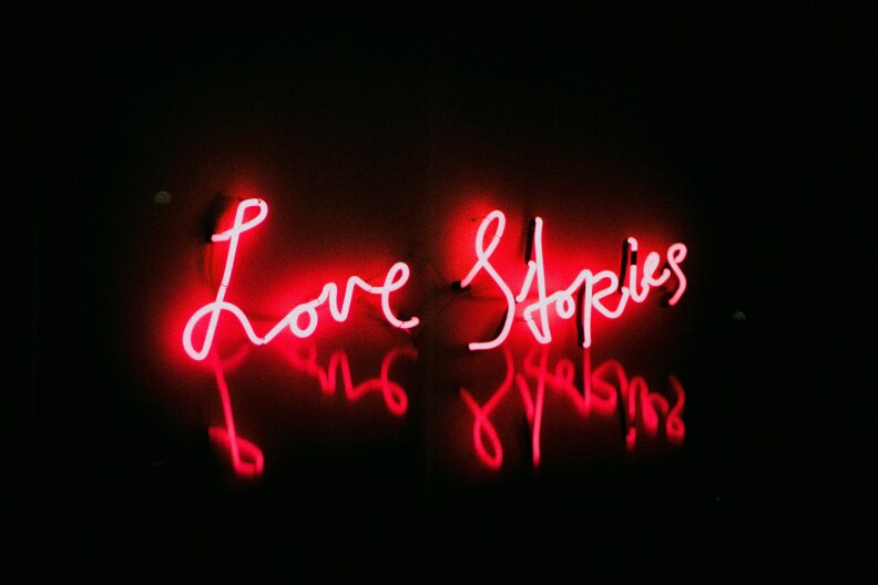 A pink neon sign reading "Love Stories" ins displayed in an otherwise black space.