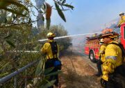 Firefighters douse flames and smoke near homes in West Hills, California on November 11, 2018, as they continue their battle to control the Woolsey Fire. - Near Los Angeles, where the fire is threatening mansions and mobile homes alike in the coastal celebrity redoubt of Malibu, the death toll has so far been limited to two victims found in a vehicle on a private driveway. (Photo by Frederic J. BROWN / AFP)        (Photo credit should read FREDERIC J. BROWN/AFP/Getty Images)