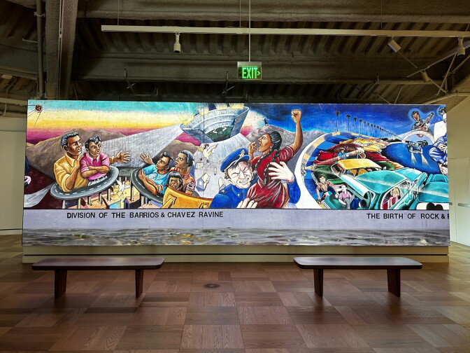 A mural depicts scenes of displacement in Chavez Ravine and vintage cars, titled 'Division of the Barrios & Chavez Ravine' and 'The Birth of Rock & Roll.'