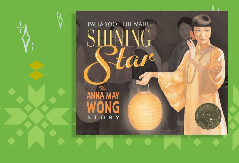 The cover of a book shows a Chinese American woman in a peach colored dress with long sleeves. There is a pink flower in her short black hair and she holds a glowing paper lantern. The title reads Shining Star: The Anna May Wong Story.